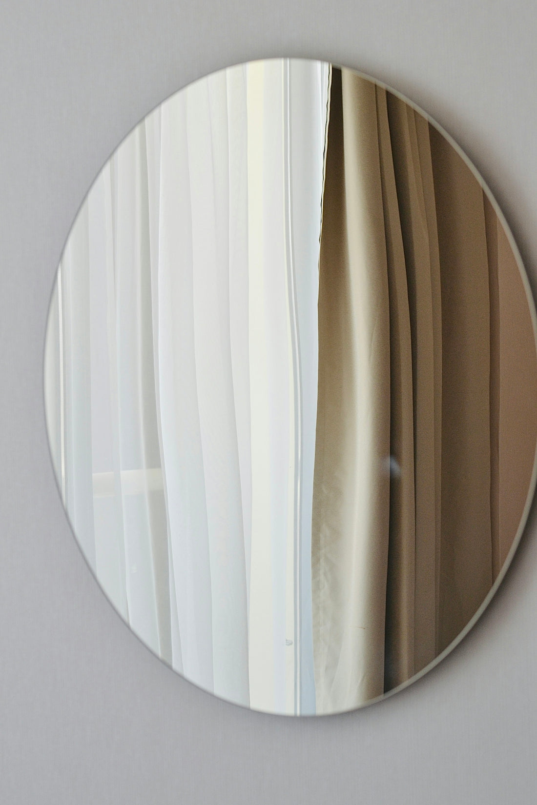 A round mirror reflects curtains.