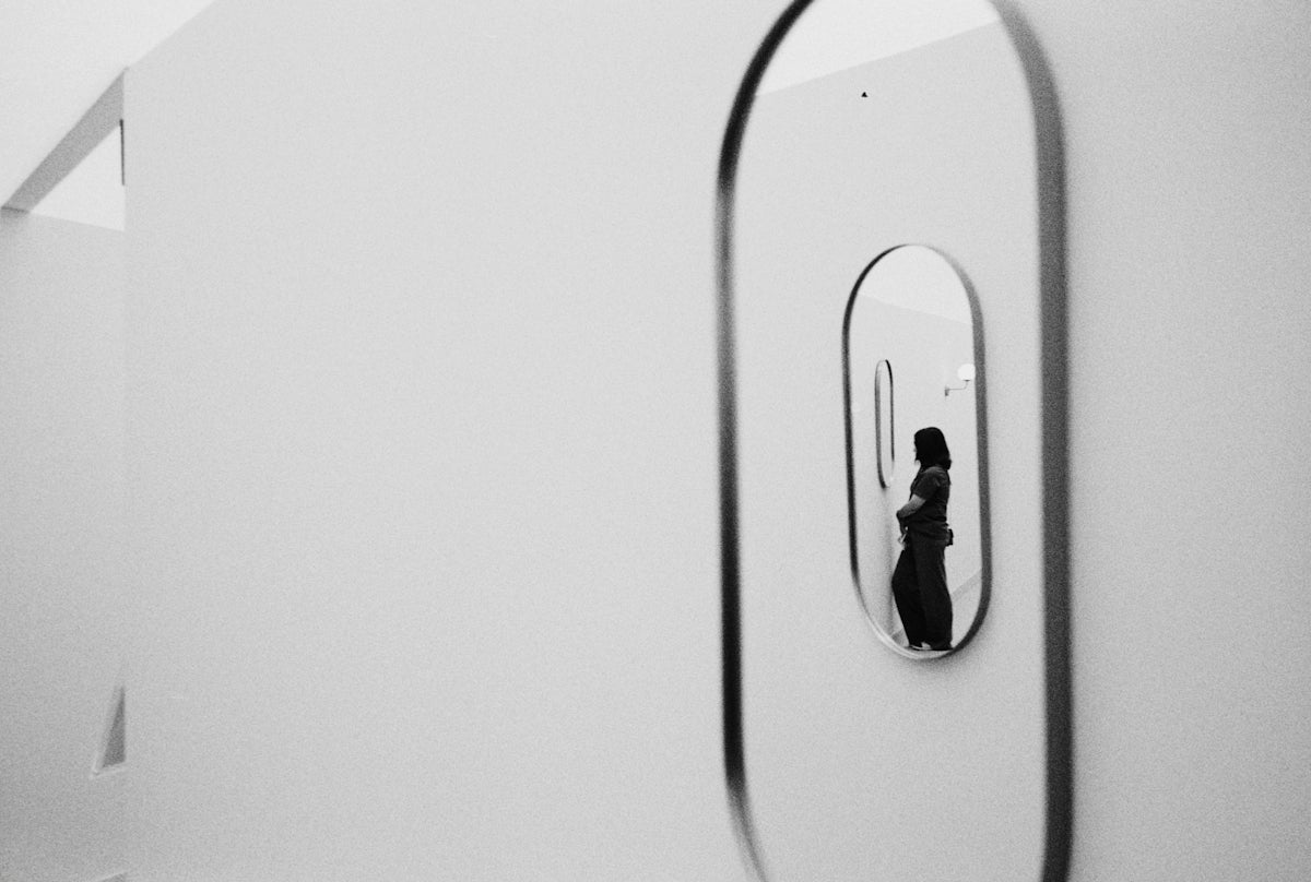 Woman reflected in an oval mirror on a white wall