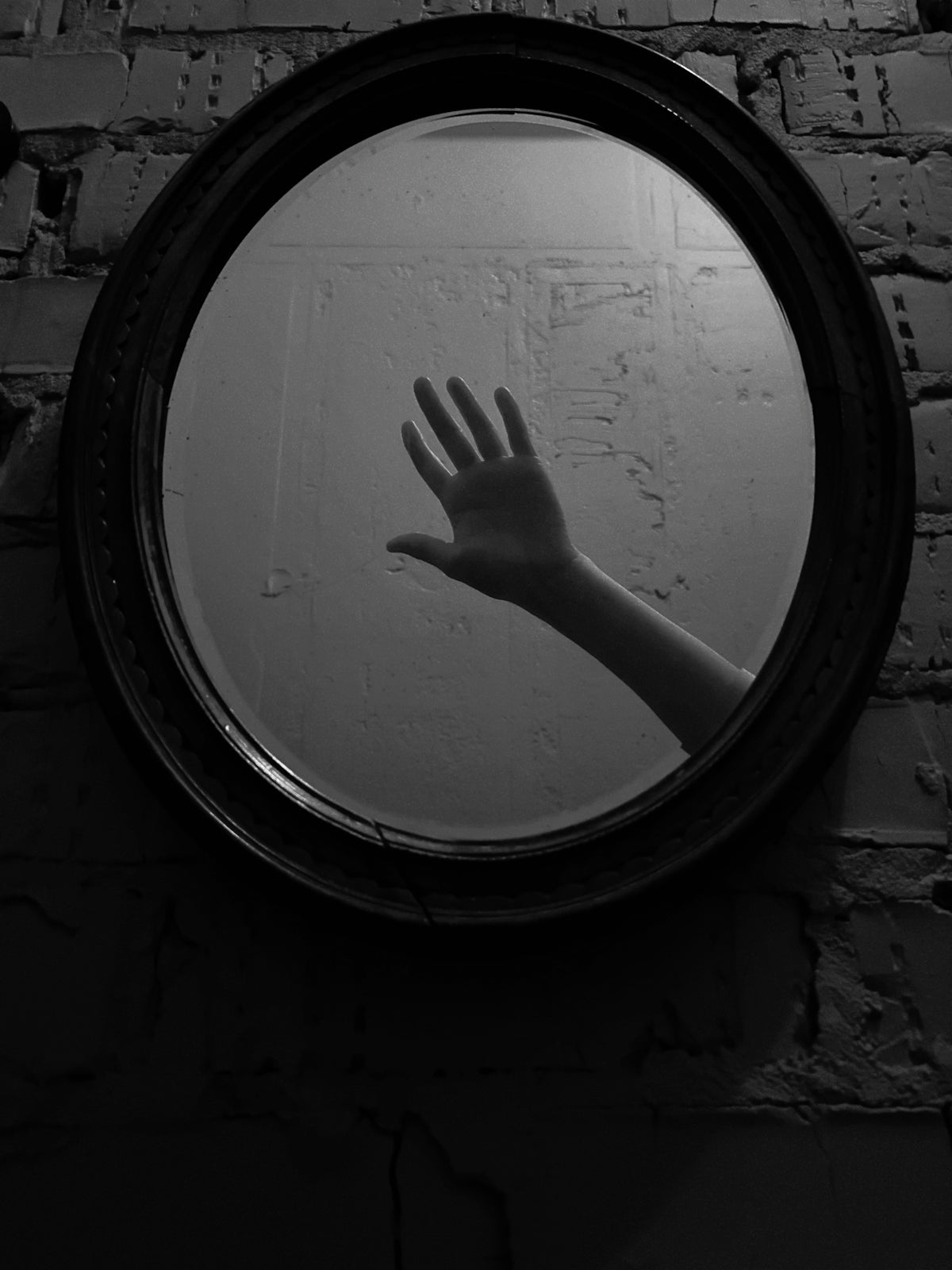 A hand reaches towards a mirror in a dark room